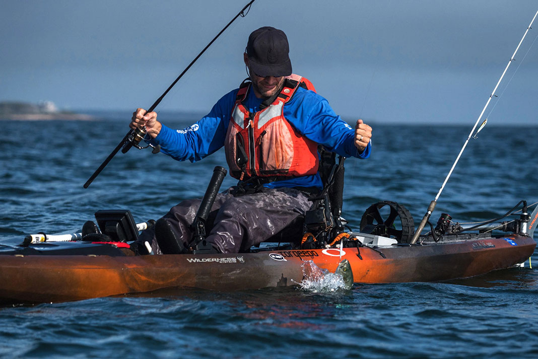a man lands a fish while wearing an orange kayak fishing life vest