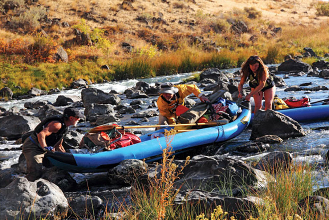 people wrangle an inflatable kayak through a rock garden on the Owyhee River
