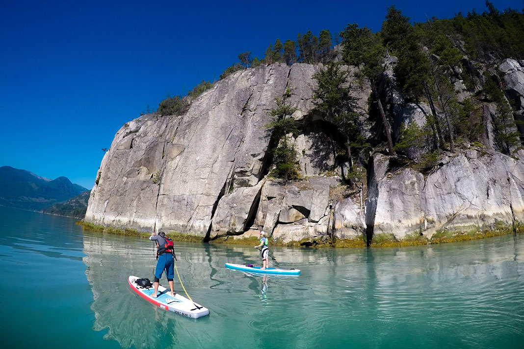 two people paddleboard past a rocky outcropping while touring Howe Sound