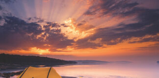 a canoe with a spray deck rests on the shores of Lake Superior along with a tent at sunset