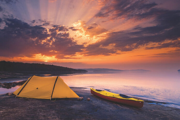 a canoe with a spray deck rests on the shores of Lake Superior along with a tent at sunset