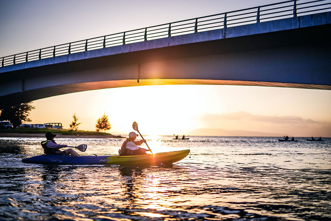 tandem kayakers pass under a bridge while paddling in urban waters