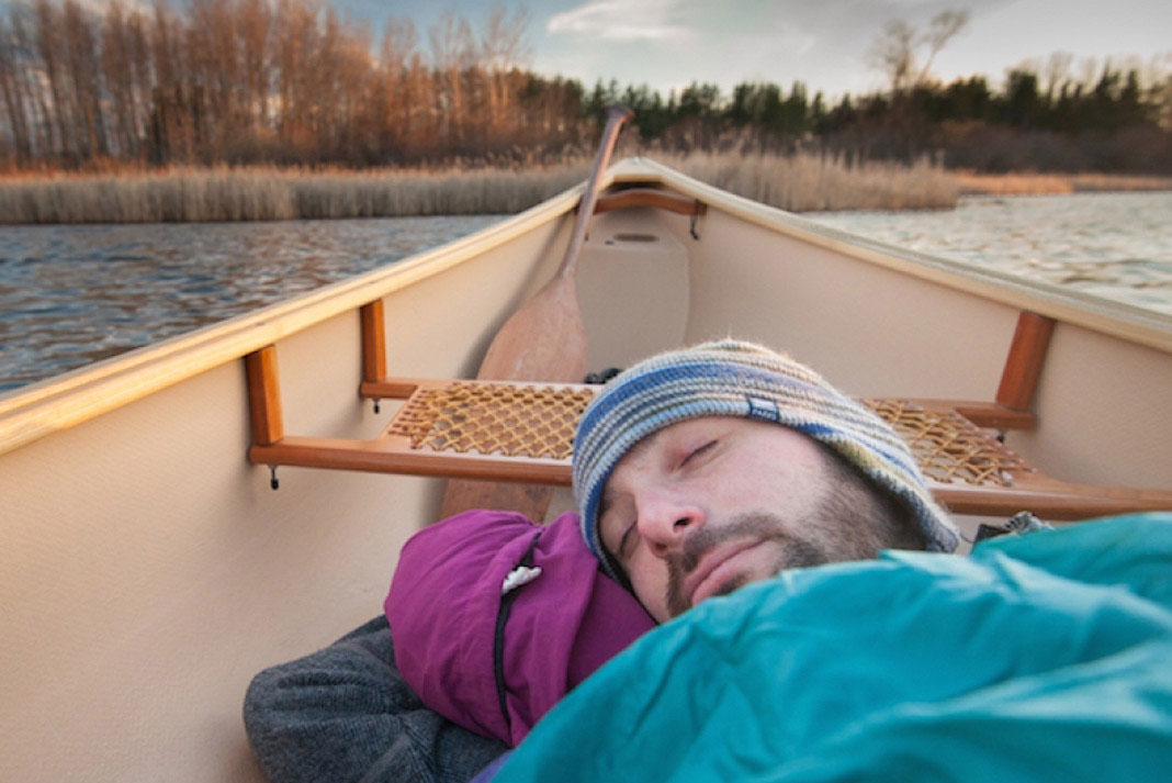 man sleeps in his canoe while on the water