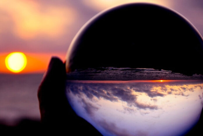 person holding up a glass orb to reflect the setting sun and some types of cloud