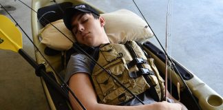 angler sleeps in a kayak while holding onto his rods and dreaming about his dream catch