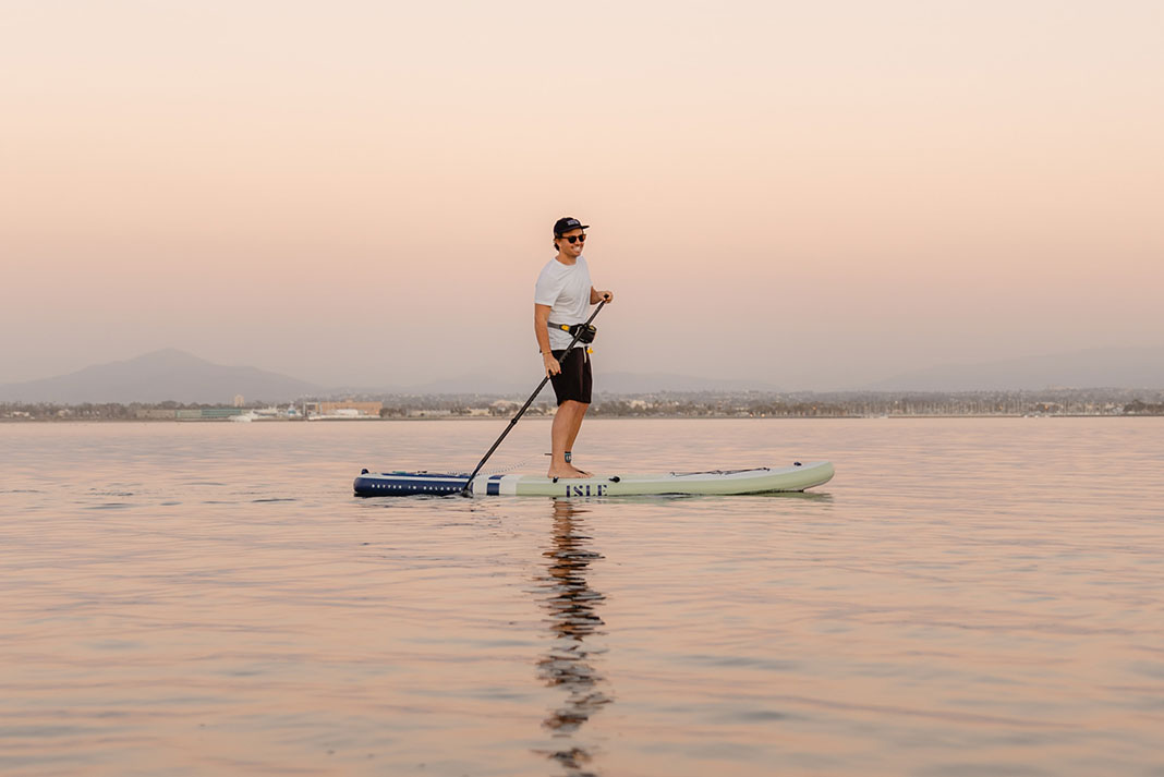man standup paddleboarding while wearing a belt pack inflatable PFD