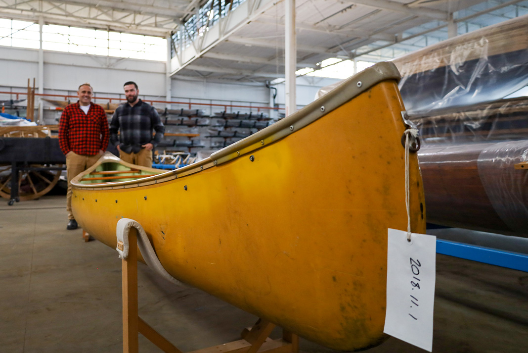 Two men standing beside a yellow canoe on a stand.