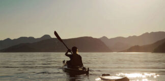 person paddles a sea kayak in British Columbia's Kyuquot Sound while towing a board for surfing