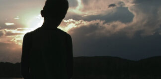 a boy stands silhouetted in front of a lake near dusk