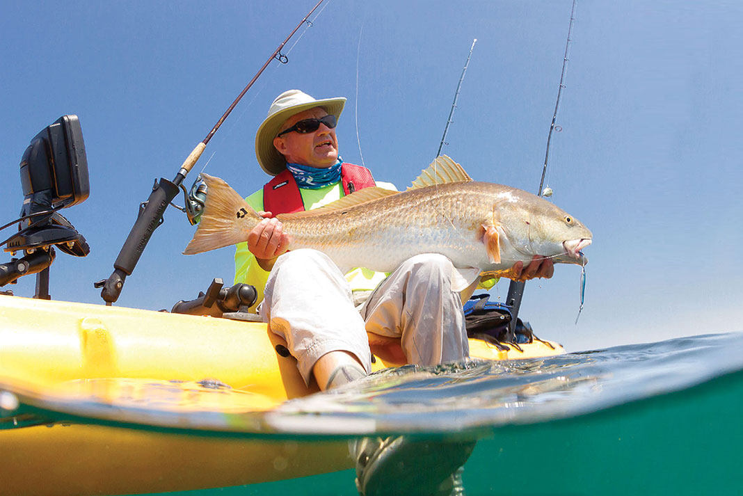 man holds up redfish caught while kayak fishing the Forgotten Coast