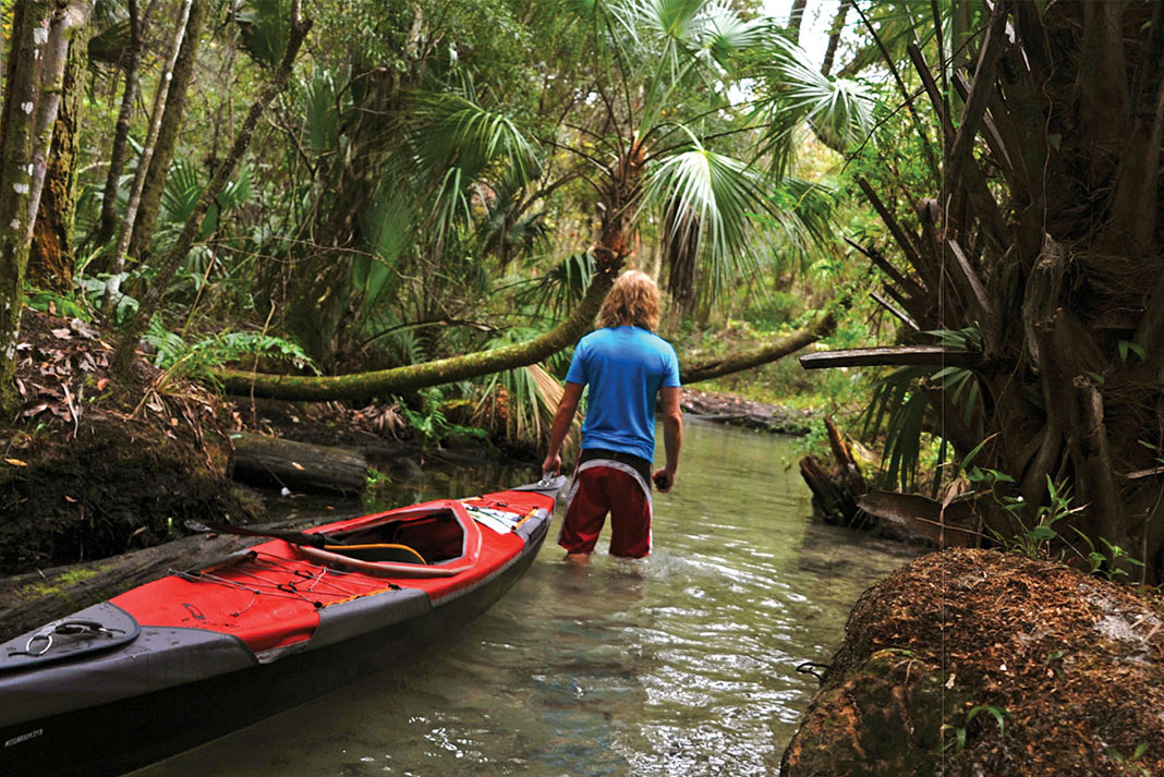man wades while pulling kayak through a Florida state park