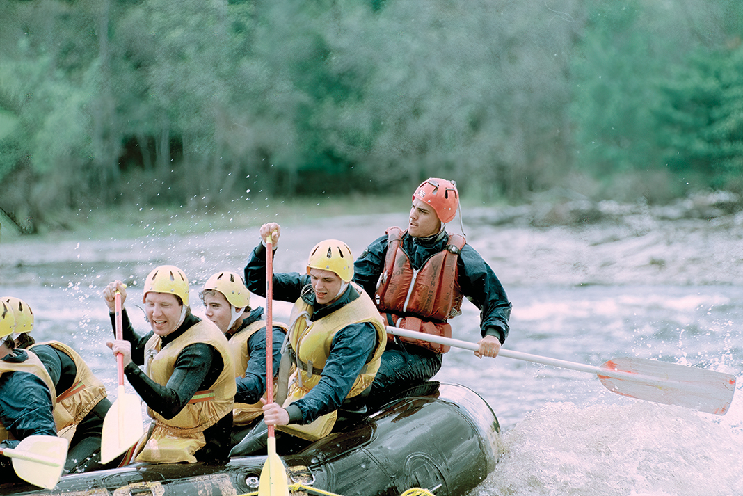 Older photo of a rafting guide paddling a raft with a whitewater rafting group