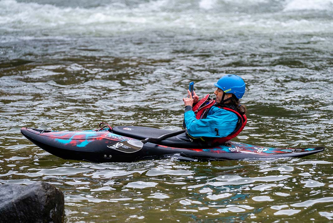 Man in whitewater kayak on his phone.