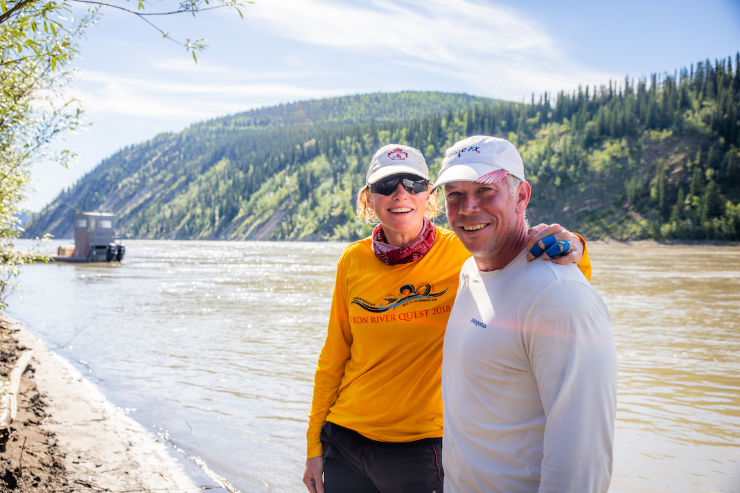 Seb and Jen Courville, the winners of the 2023 Yukon River Quest, standing beside the Yukon River after finishing the race.