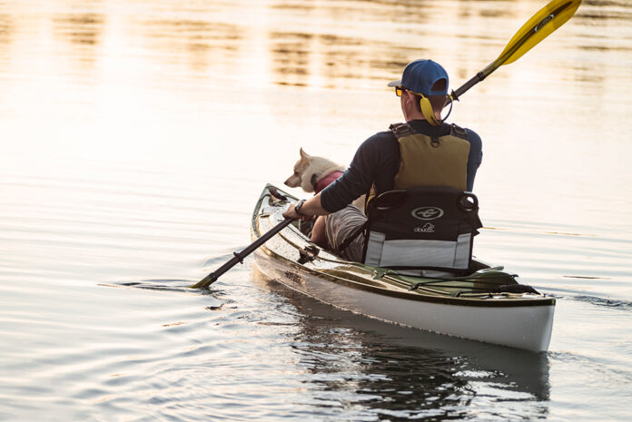 man paddles a kayak with his dog sitting in the bow