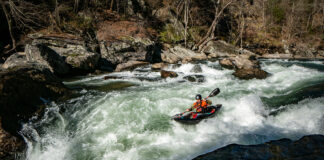 person paddles a kayak down a whitewater river run