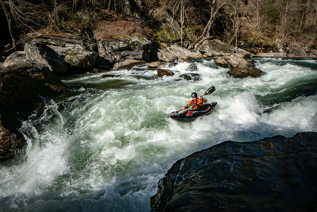 person paddles a kayak down a whitewater river run