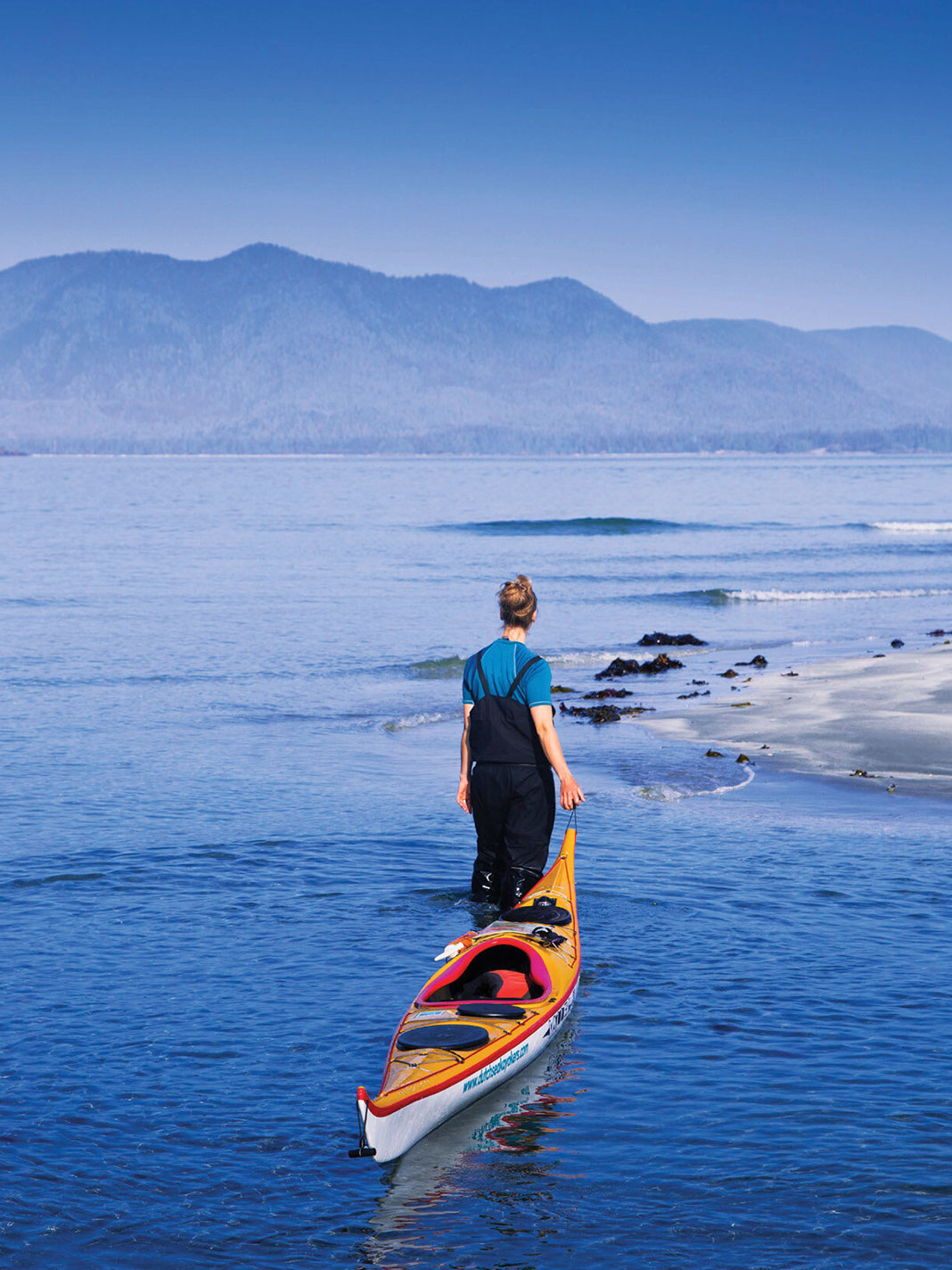 woman wading with kayak looks out across Clayoquot Sound