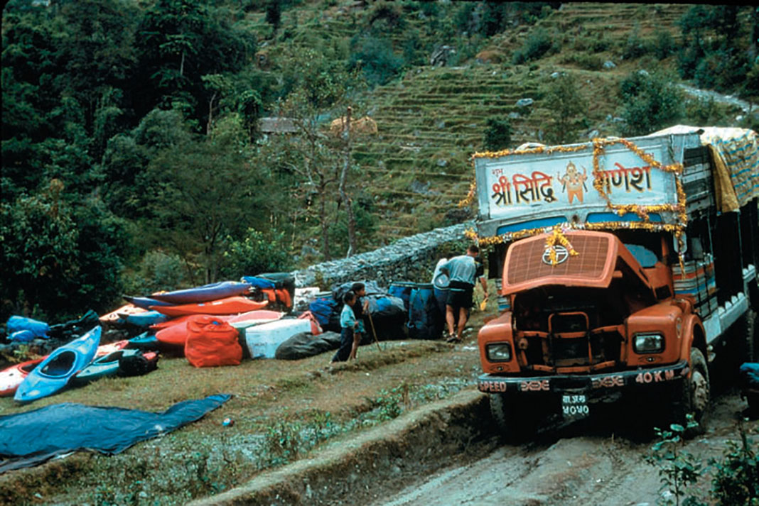 a group of whitewater kayaks sit at the roadside near a bus on the Tamur River in Nepal