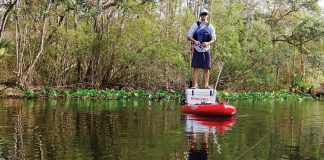 man stands on his kayak cooler and fishes with a topwater lure