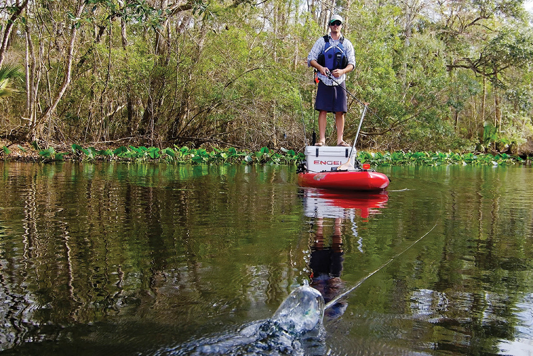 man stands on his kayak cooler and fishes with a topwater lure