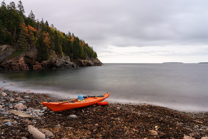 a touring kayak sits on a rocky beach in fall