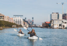 Two people paddling folding kayak on an urban waterway.