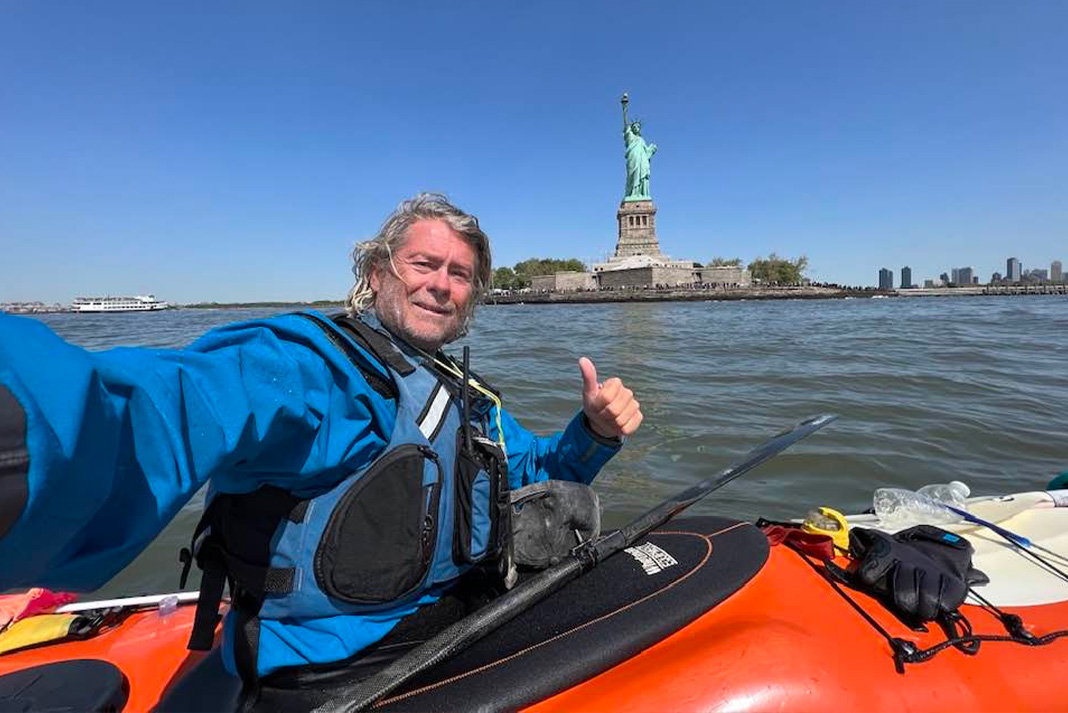 Mark Ervin giving a thumbs up from his red sea kayak in front of the Statue of Liberty.