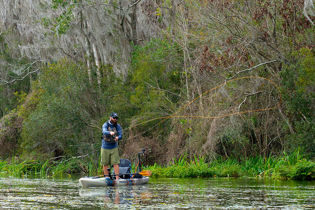 bearded man standing and casting while fly fishing from a kayak