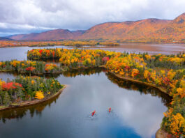 two touring kayakers paddle through a picturesque lake in fall