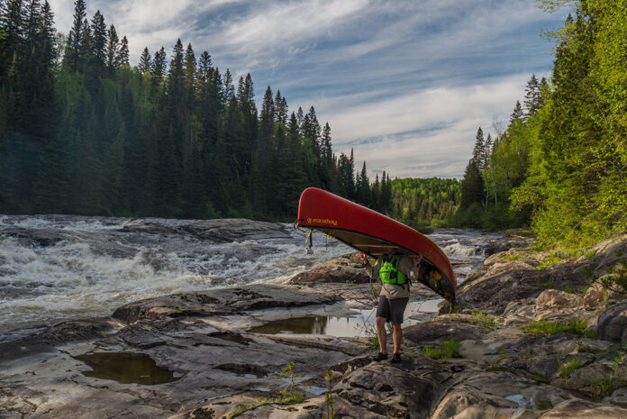 person portages a Prospector canoe along the banks of a raging river