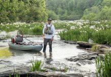 man wades down a river with his fishing kayak