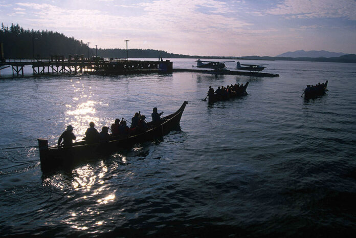 a group of people silhouetted while they paddle traditional dugout canoes