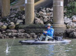 Man sits and fishes from the Bonafide P127 pedal fishing kayak near concrete bridge supports