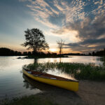 Need For Speed: How Racing Changed Canoeing For The Better a canoe with design features borrowed from the racing world sits on a sandy bank at dusk