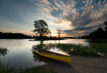 a canoe with design features borrowed from the racing world sits on a sandy bank at dusk