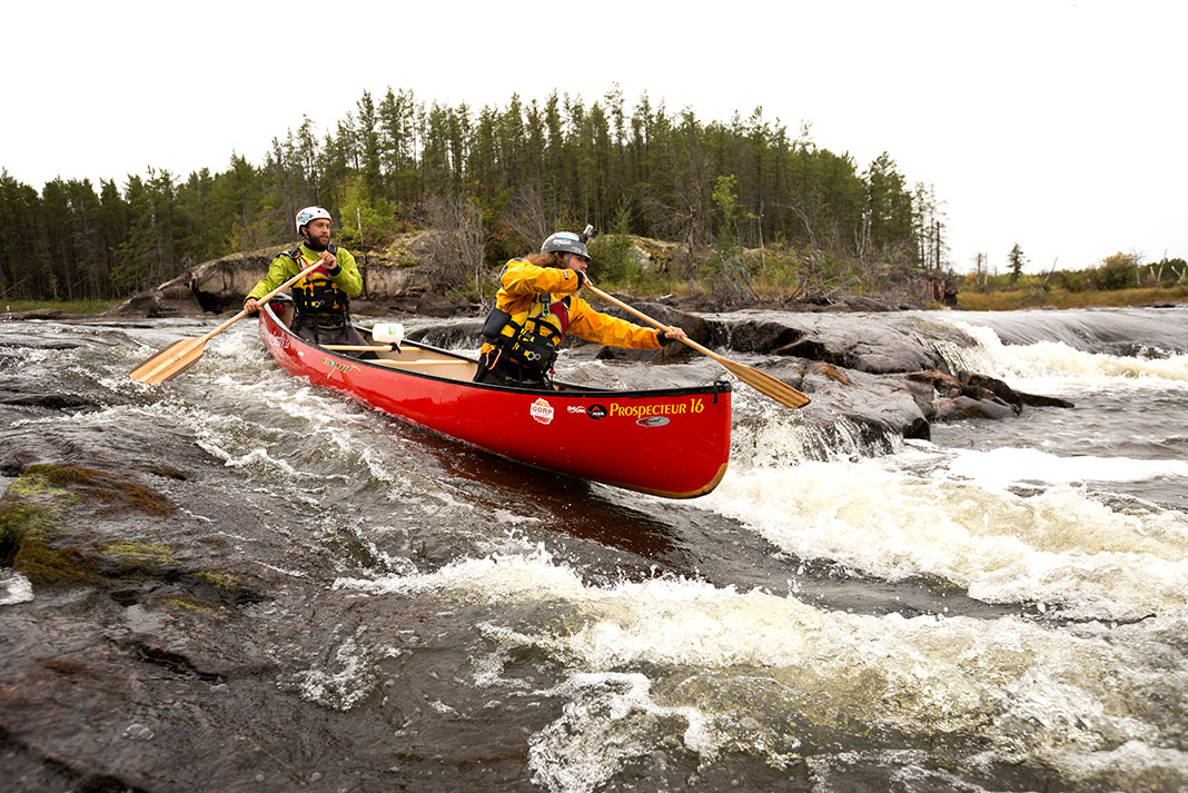 two men paddle a canoe through whitewater