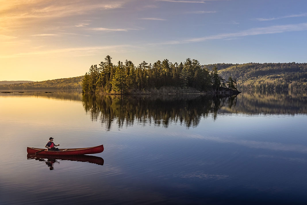 a person solo paddling a canoe across a very still lake