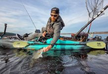 man lands fish from his fishing kayak with paddle strapped to the side