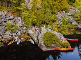 a group of canoe trippers stand on a riverside boulder for their morning meeting