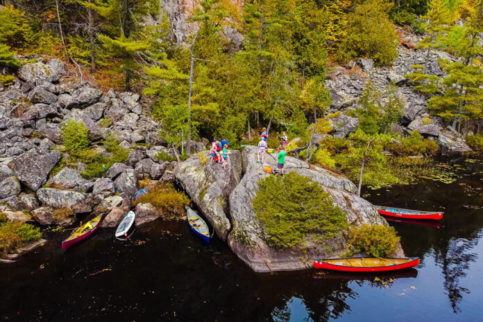a group of canoe trippers stand on a riverside boulder for their morning meeting
