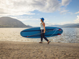 woman carrying a paddleboard equipped with fins across a sandy beach
