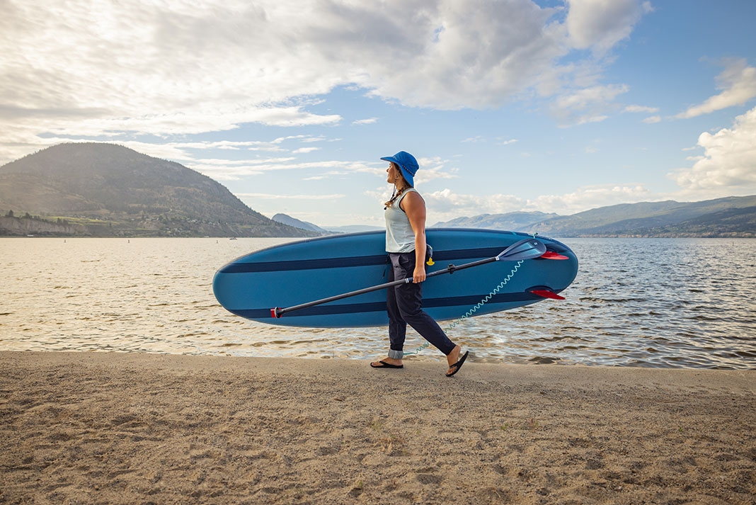 woman carrying a paddleboard equipped with fins across a sandy beach