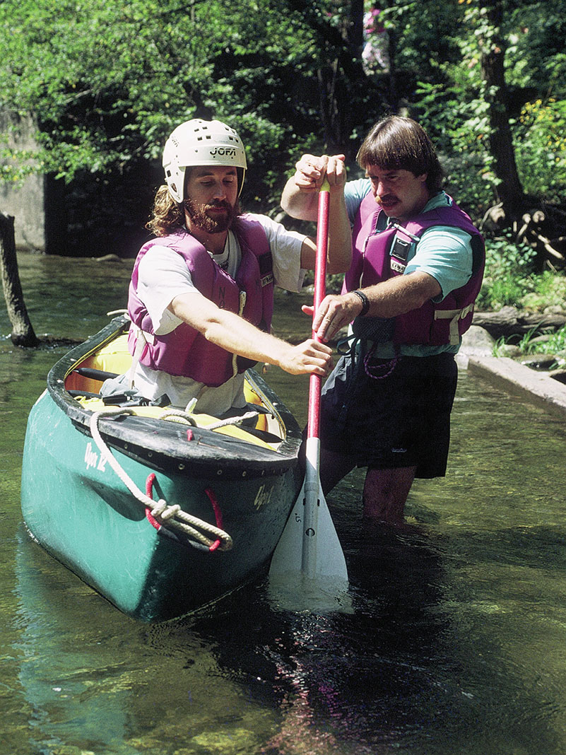 An instructor with an early paddlesports trade group shows a student how to paddle a canoe