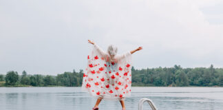 a person jumping at the end of a dock while wearing a maple leaf poncho in rainy weather