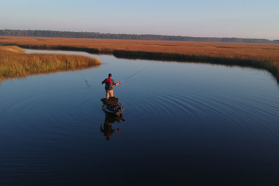 man stands on his kayak and casts for redfish on calm, glassy grass flats
