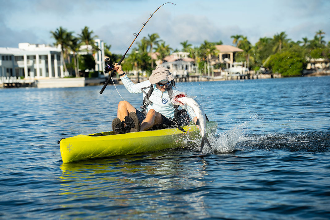 man reels in a thrashing tarpon while fishing from a yellow kayak in Florida