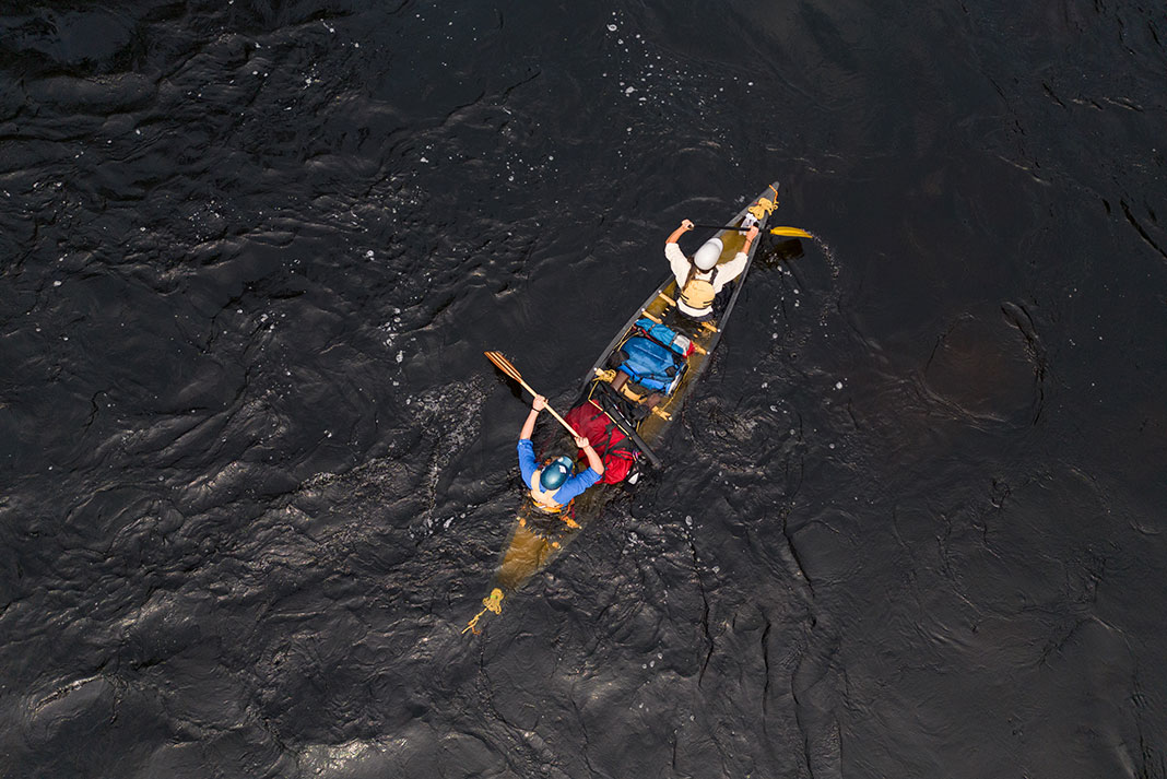 overhead view of two people paddling a flooded tripping canoe on black water in Wabakimi