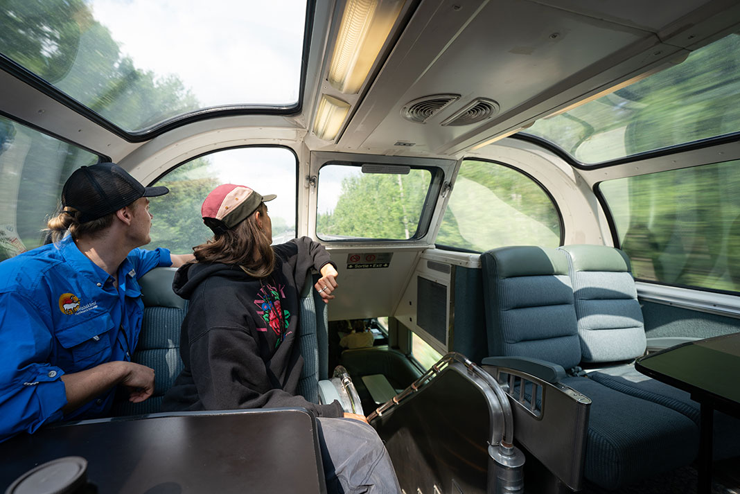 two people look out the window on a train into Wabakimi Provincial Park