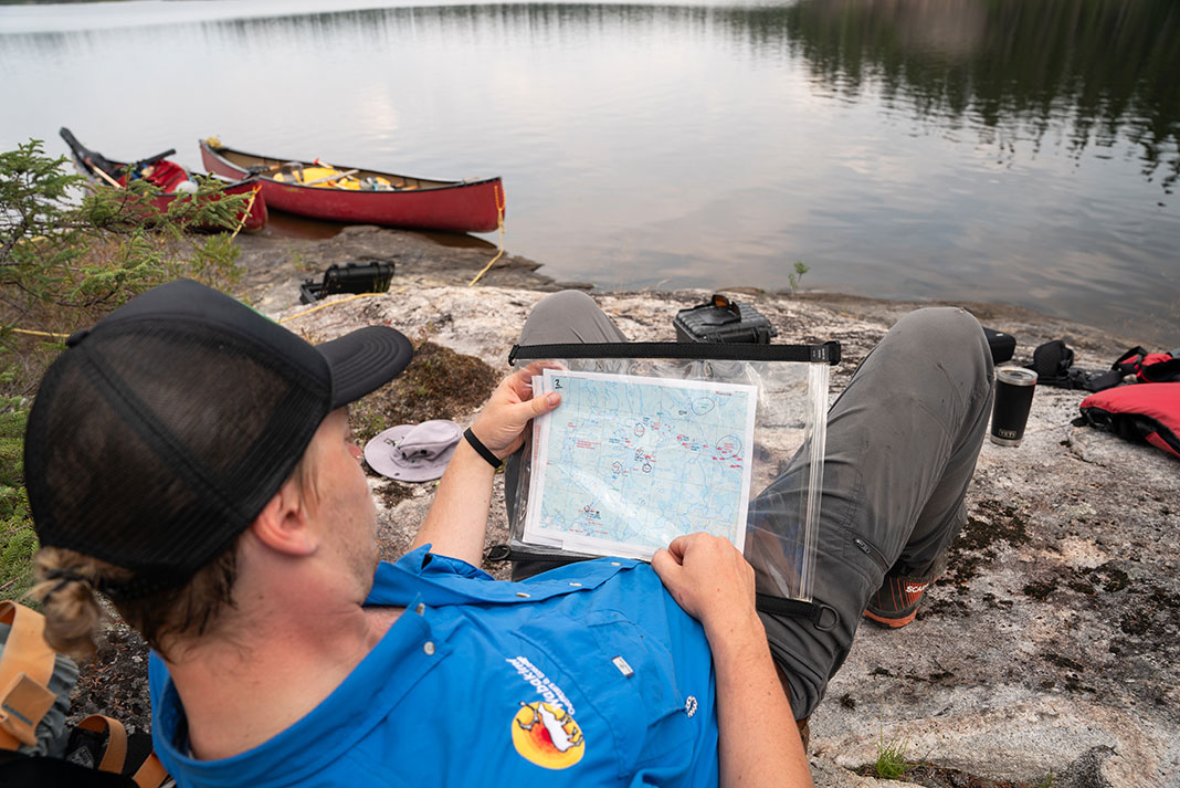 Wabakimi Outfitters guide reclines and looks at a map at a waterside campsite